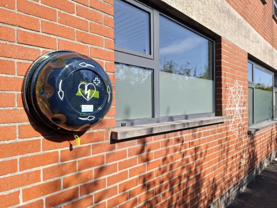 Automatische externe defibrillator (AED) aan een bakstenen muur naast ramen met een spinnenwebtekening. (vergroot foto)